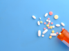 Pills spill out from an orange prescription bottle on a blue background